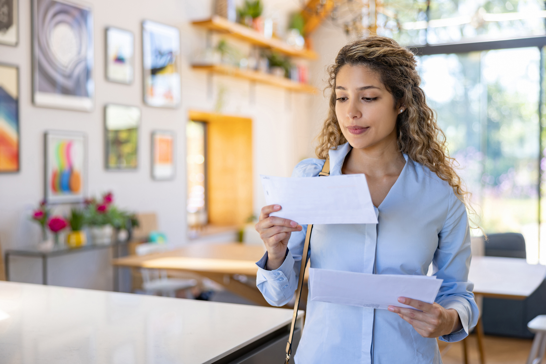 A young woman looks an an envelope inside her home, looking deep in thought.