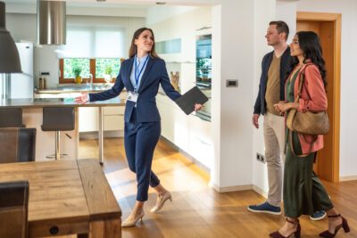 A female real estate agent shows a young couple around a property.