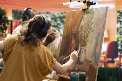 Diverse painters applying watercolor paint with brushstrokes for a certain technique, working together on colorful artwork creation for the gallery. Man and woman enjoying artistic hobby.