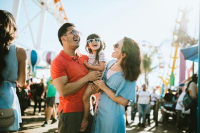 A cute mixed race family enjoys the rides and sun at the fair activities on Santa Monica Pier in Los Angeles, California. They all wear sunglasses with big smiles.